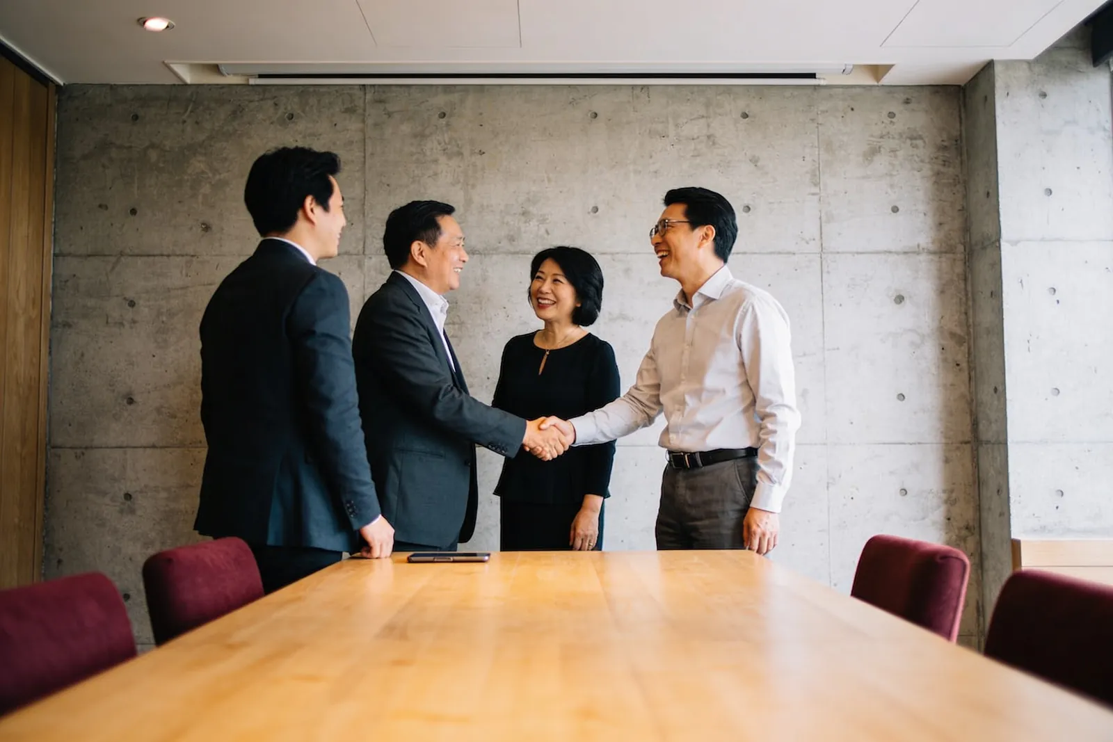 例會開始前的包廂裡，一位成員把兩個人介紹給彼此，兩人正在握手，旁邊的人笑著看。